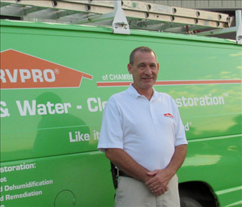 A male with brown hair, white shirt standing in front of the Green SERVPRO van. 